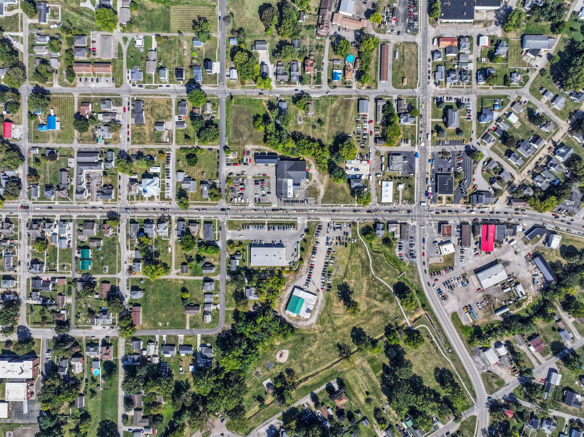 Aerial view of a suburban town with streets, houses, green spaces, and commercial buildings.